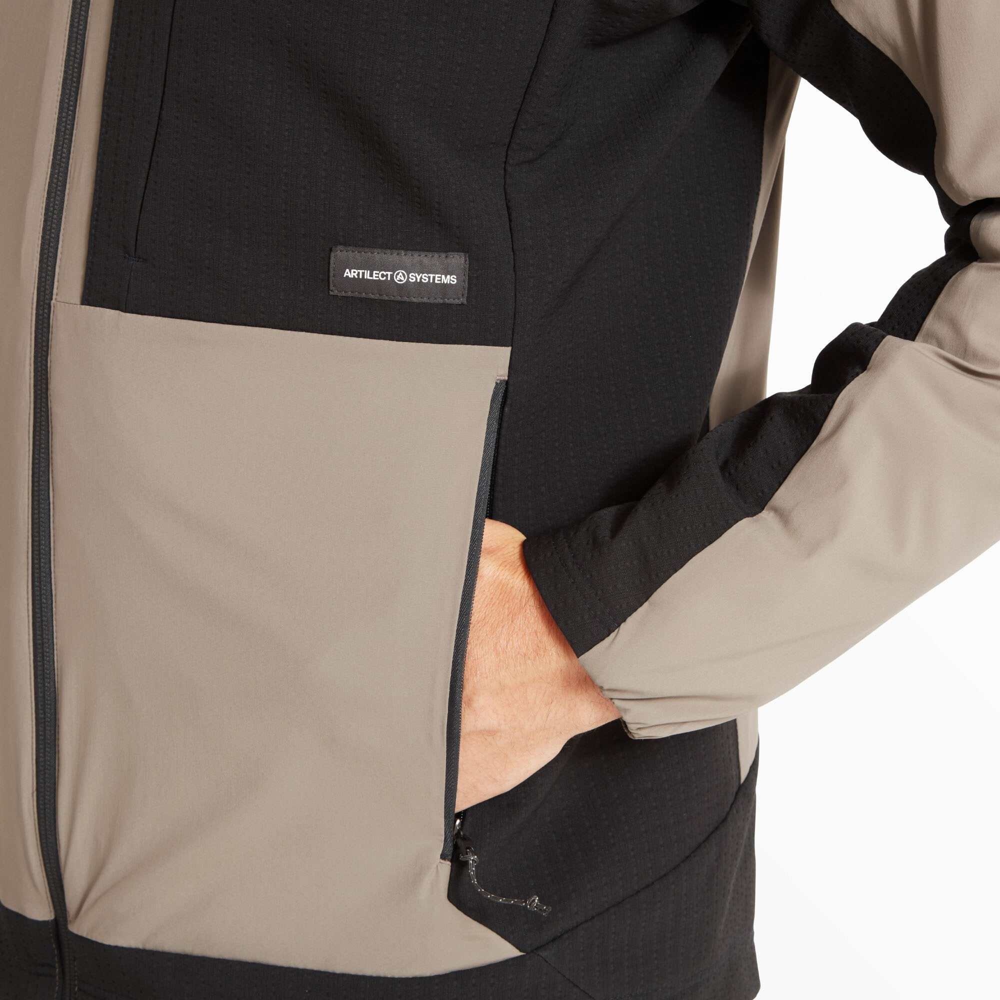 Detail image showing the model’s hand in the side pocket. The Artilect Performance Mens Darkstart Fusion Jacket Black features black lower panels with an Artilect Systems logo label and a vertical zipper on the pocket.