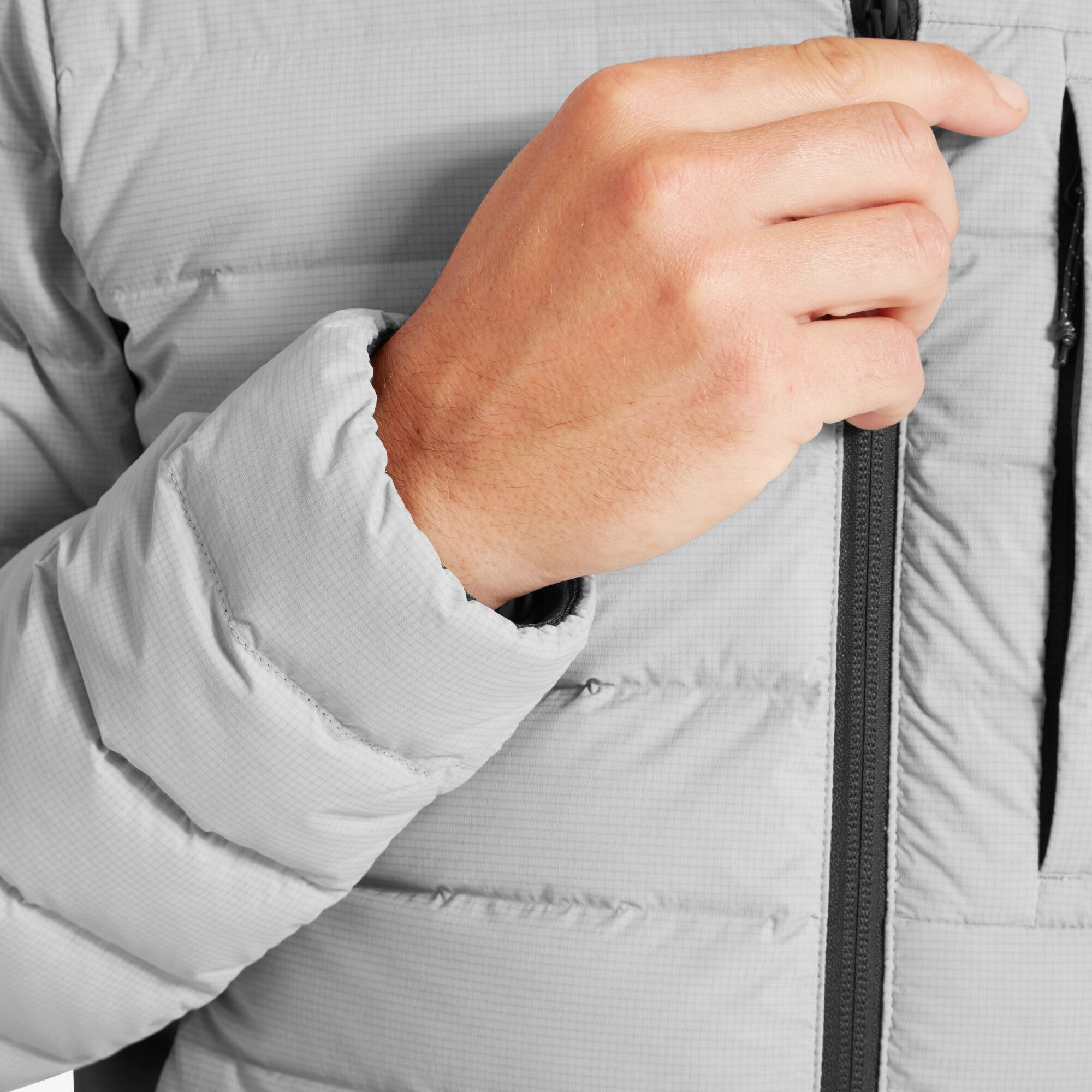 Close-up of the model’s right hand near the main zipper, focusing on the cuff of the quilted sleeve and the textured, easy-grip zipper pull on the Artilect Performance Mens Divide Fusion Stretch Hoodie Grey.