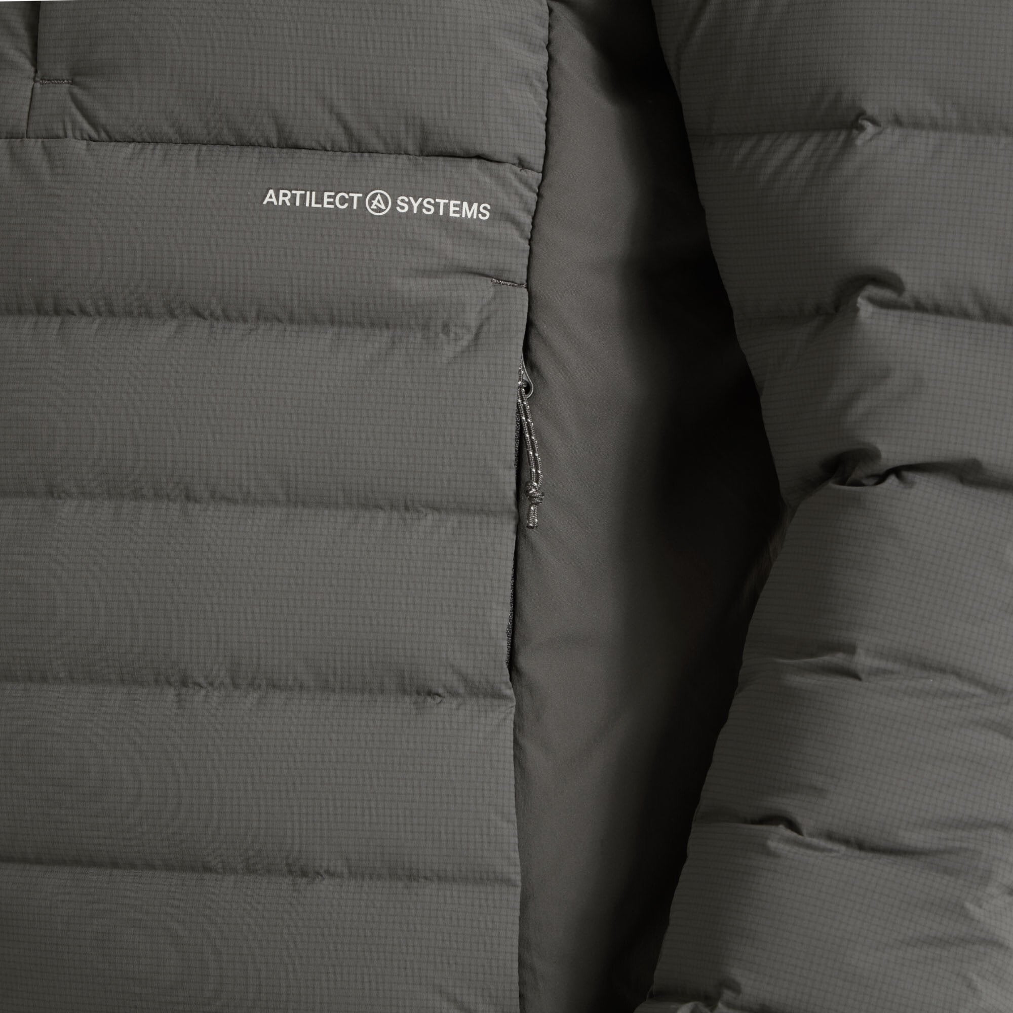 A close-up of the Artilect Performance Mens Divide Fusion Stretch Jacket Grey’s left side, highlighting the “ARTILECT SYSTEMS” logo above the left-hand zipper pocket. The texture of the shell fabric and zipper detailing are also clearly shown.
