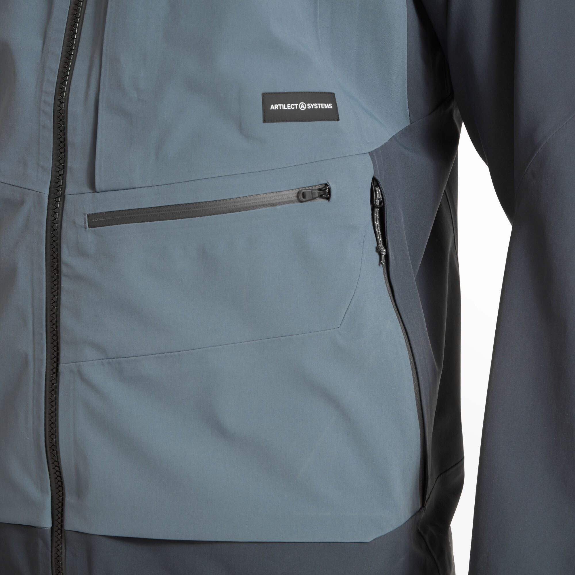Close-up of the lower section of the Artilect Performance Mens Formation 3L Jacket Blue showing dual zippered waist pockets and the Artilect Systems branding patch on the left chest, with fabric texture and stitching clearly visible.