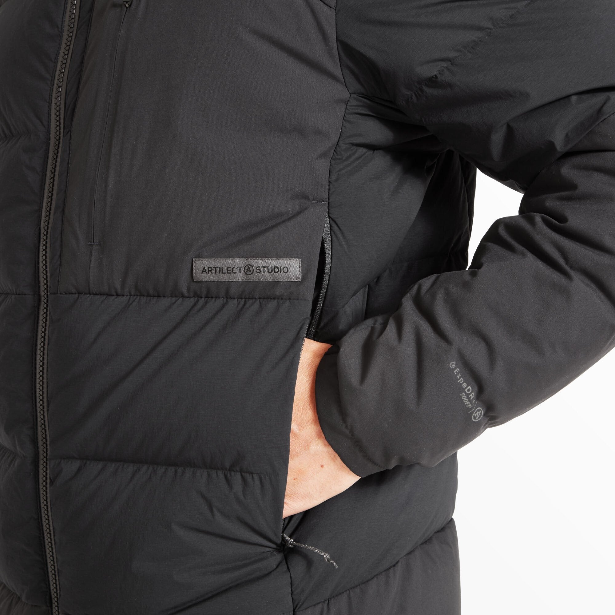 Close-up of the model's hand tucked into the right side pocket on the Artilect Performance Mens High AF Down Stretch Parka Black. Visible is a rubberized Artilect Studio logo patch above the pocket, and subtle branding on the sleeve indicating “GEOPOWER 20K/20K” waterproof performance.