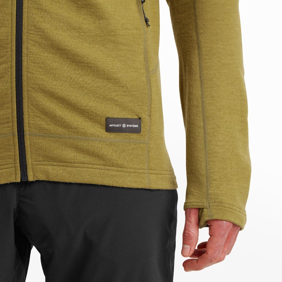A detailed image of the lower left side of the Artilect Performance Mens Quandary Peak Hoodie Green focuses on the ARTILECT SYSTEMS logo patch above the hem and a thumbhole in the cuff of the sleeve.