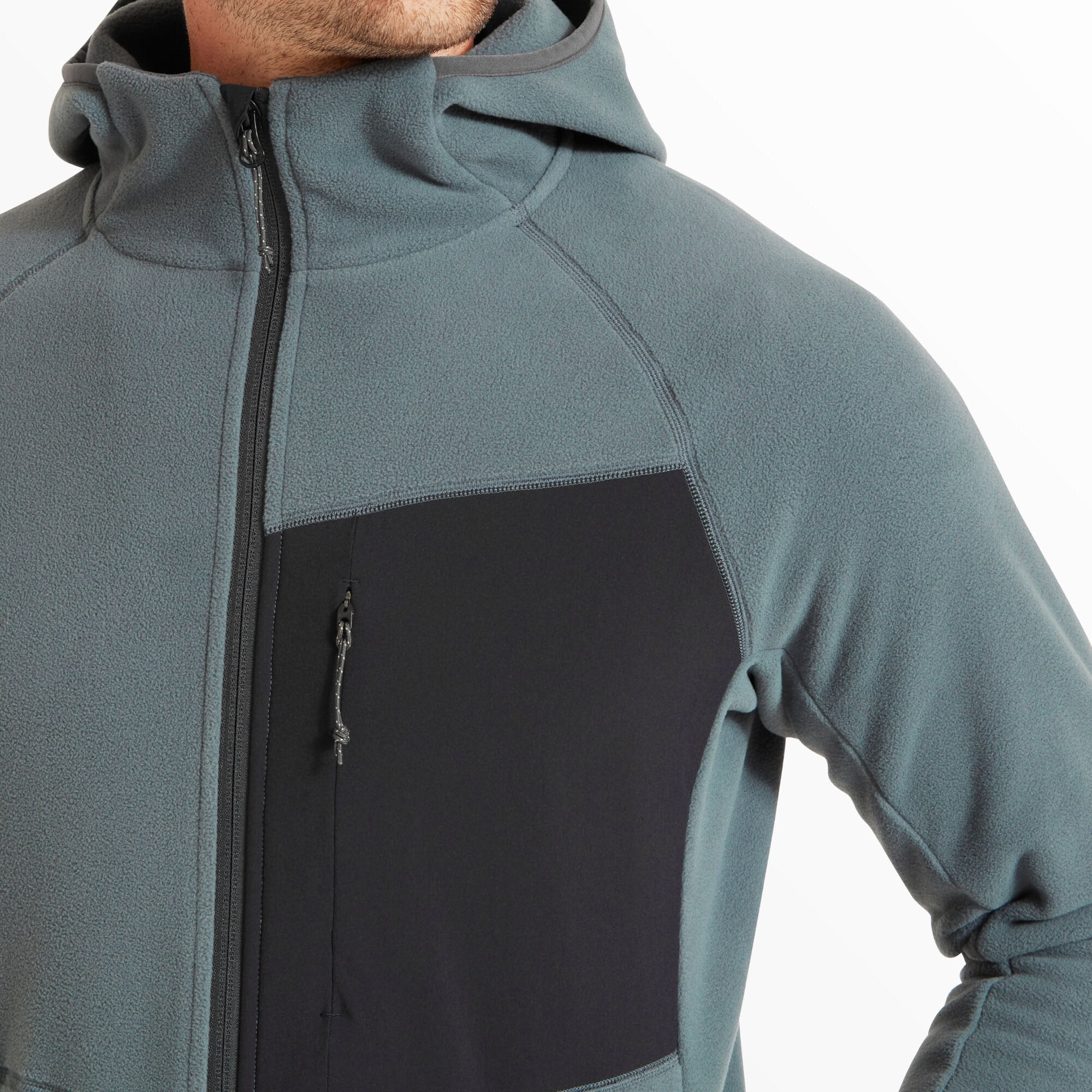 A zoomed-in image of the upper torso highlights the black chest panel with a vertical zip pocket on the Artilect Performance Mens Supermoon Bio Hoodie Blue. The seam work and contrast stitching are clean and precise, emphasizing the technical construction.
