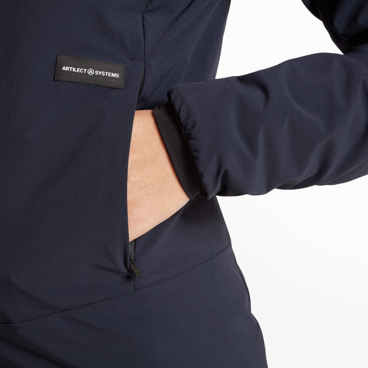Detail of the lower right side of the Artilect Performance Womens Elevate Primaloft Bio Insulated Hoodie Blue where the wearer’s hand is in the zippered side pocket. The "ARTILECT SYSTEMS" label is stitched next to the pocket.