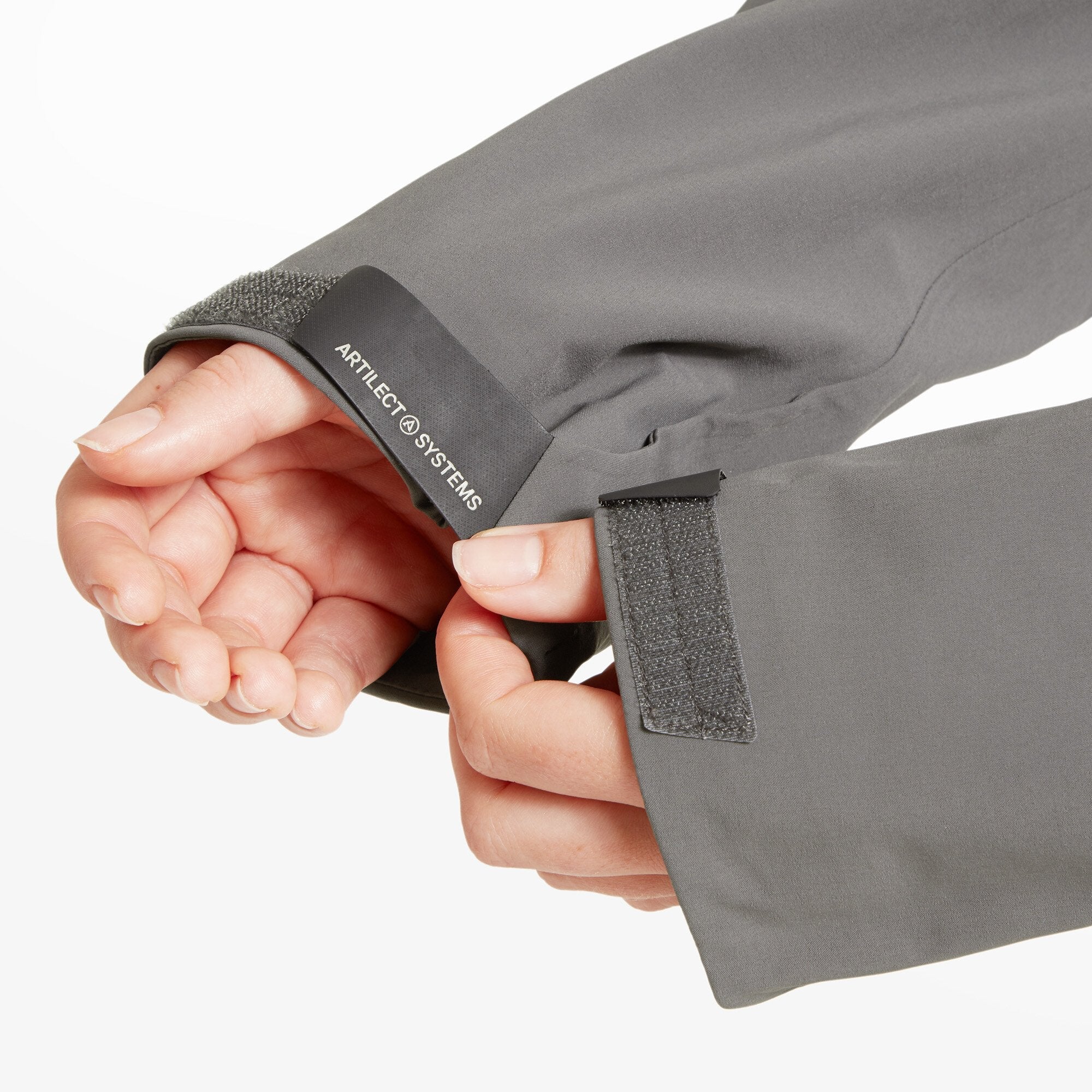 A close-up showing the wrist cuff area on the Artilect Performance Womens Formation 3L Jacket Grey. The model’s hand adjusts the hook-and-loop (Velcro) closure, revealing the printed Artilect Systems name on the inside of the cuff.