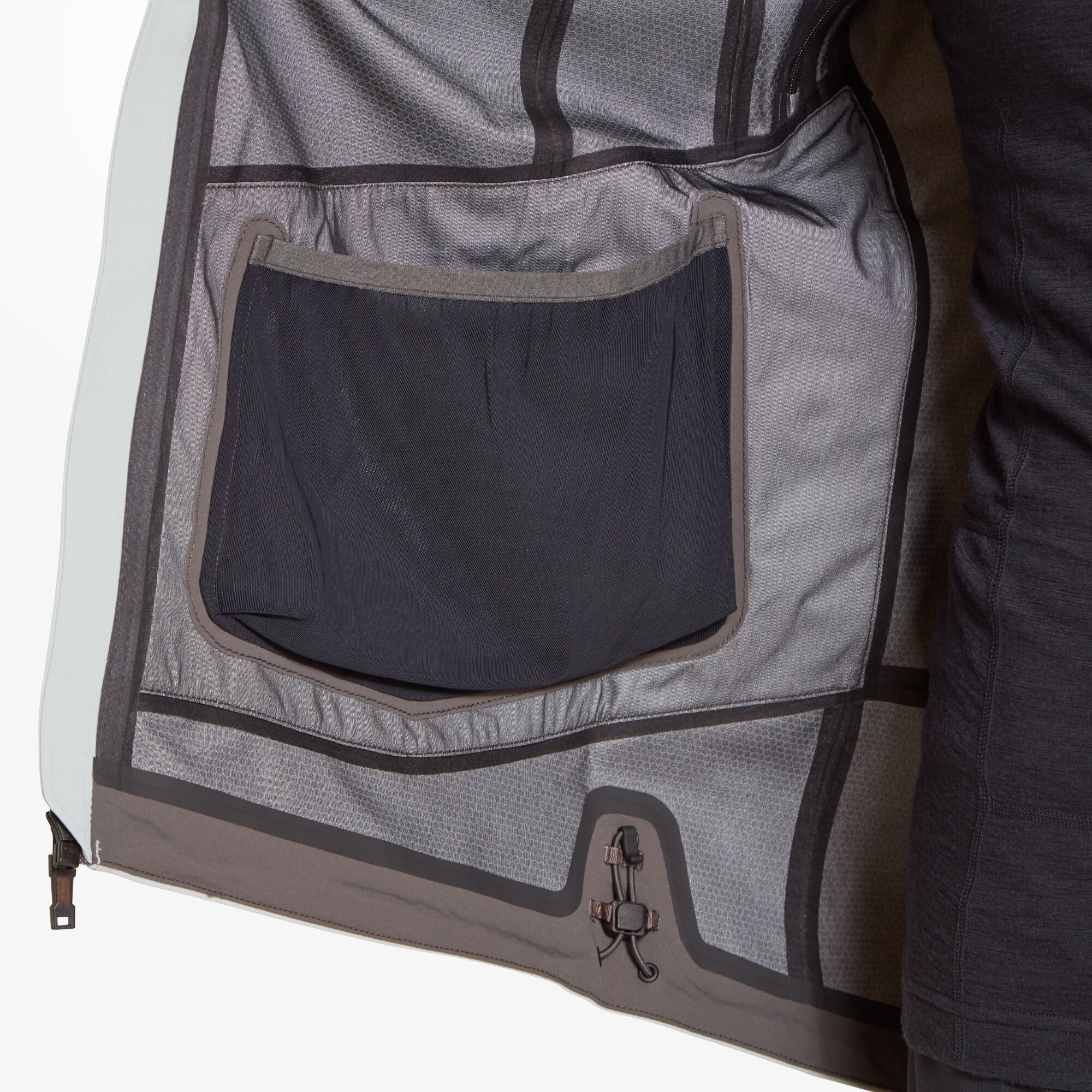 The inside of the Artilect Performance Womens Formation 3L Jacket Grey is shown with one side opened to reveal a black mesh drop-in pocket and taped seam construction; a cinch cord is located near the hem for waist adjustment.