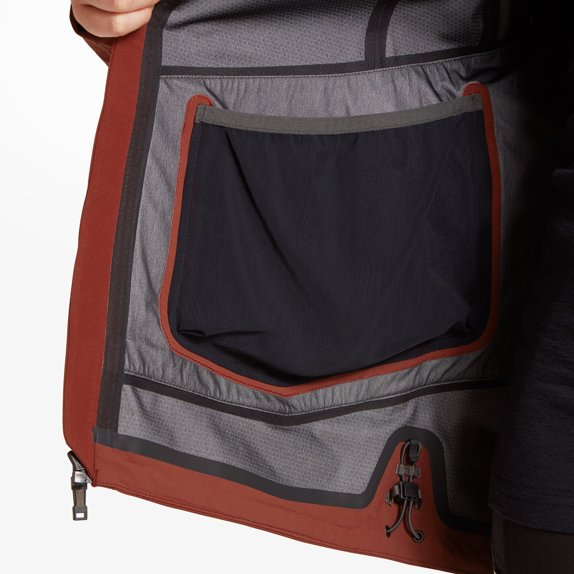 A view of the inside of the Artilect Performance Womens Formation 3L Jacket Orange showing the internal mesh pocket and seam taping; the model holds the jacket open to reveal construction and storage design features.