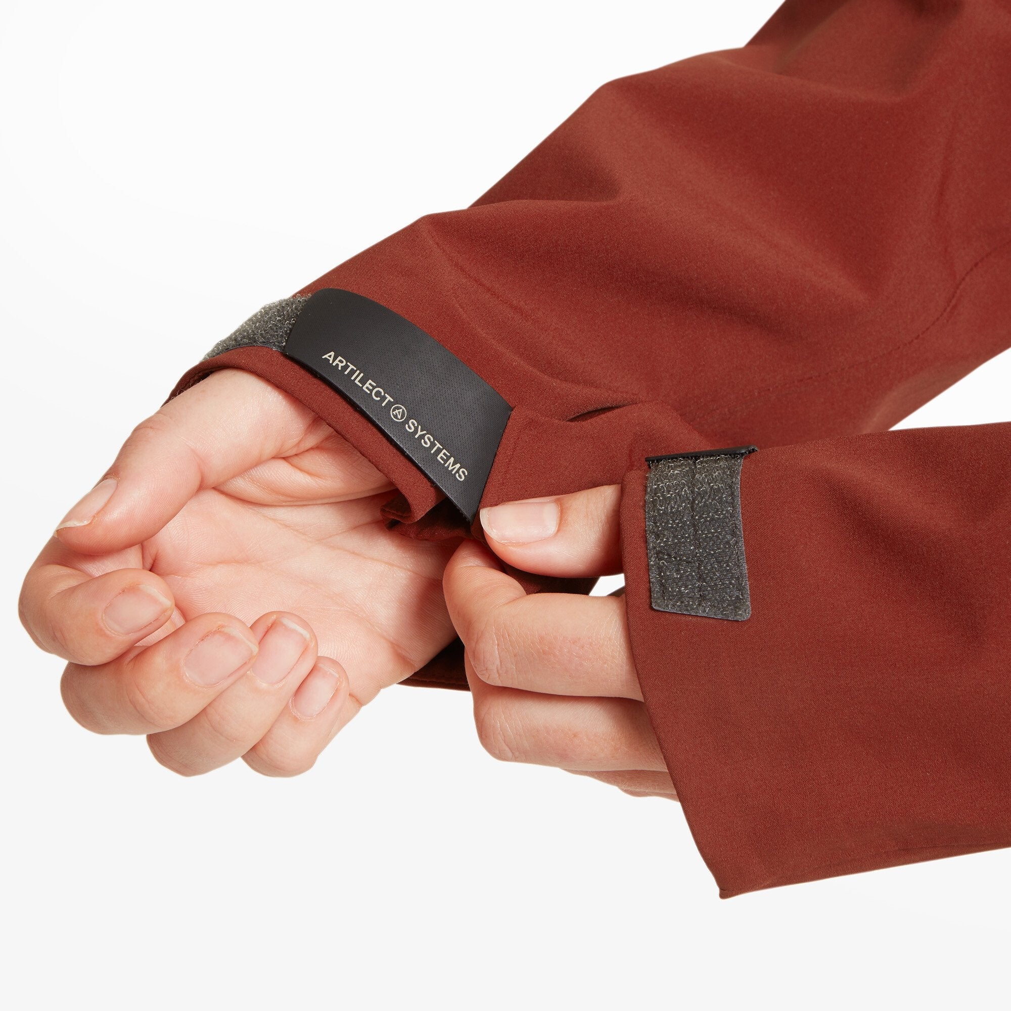 A close-up of the sleeve cuff on the Artilect Performance Womens Formation 3L Jacket Orange, showing the Artilect Systems logo on the black trim and the Velcro adjustment tab being secured by the model.