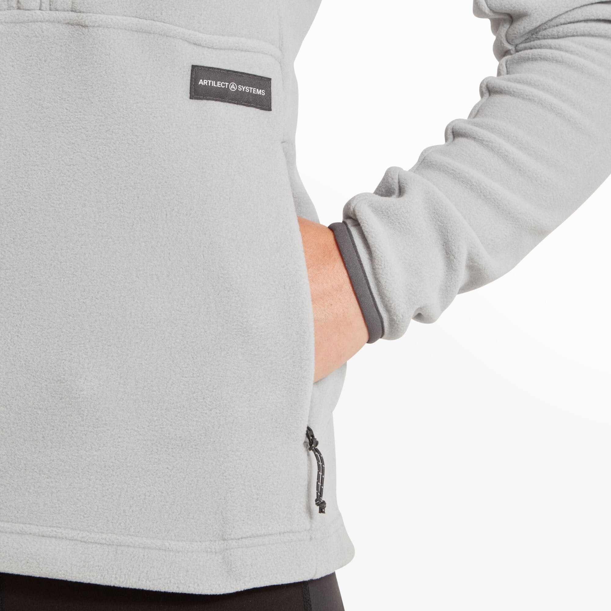 Close-up view of the right-hand pocket area on the Artilect Performance Womens Halfmoon Bio Pullover Grey. The model’s hand is partially inside the pocket, with the "ARTILECT SYSTEMS" label sewn nearby, showcasing the pocket construction and soft fleece material.
