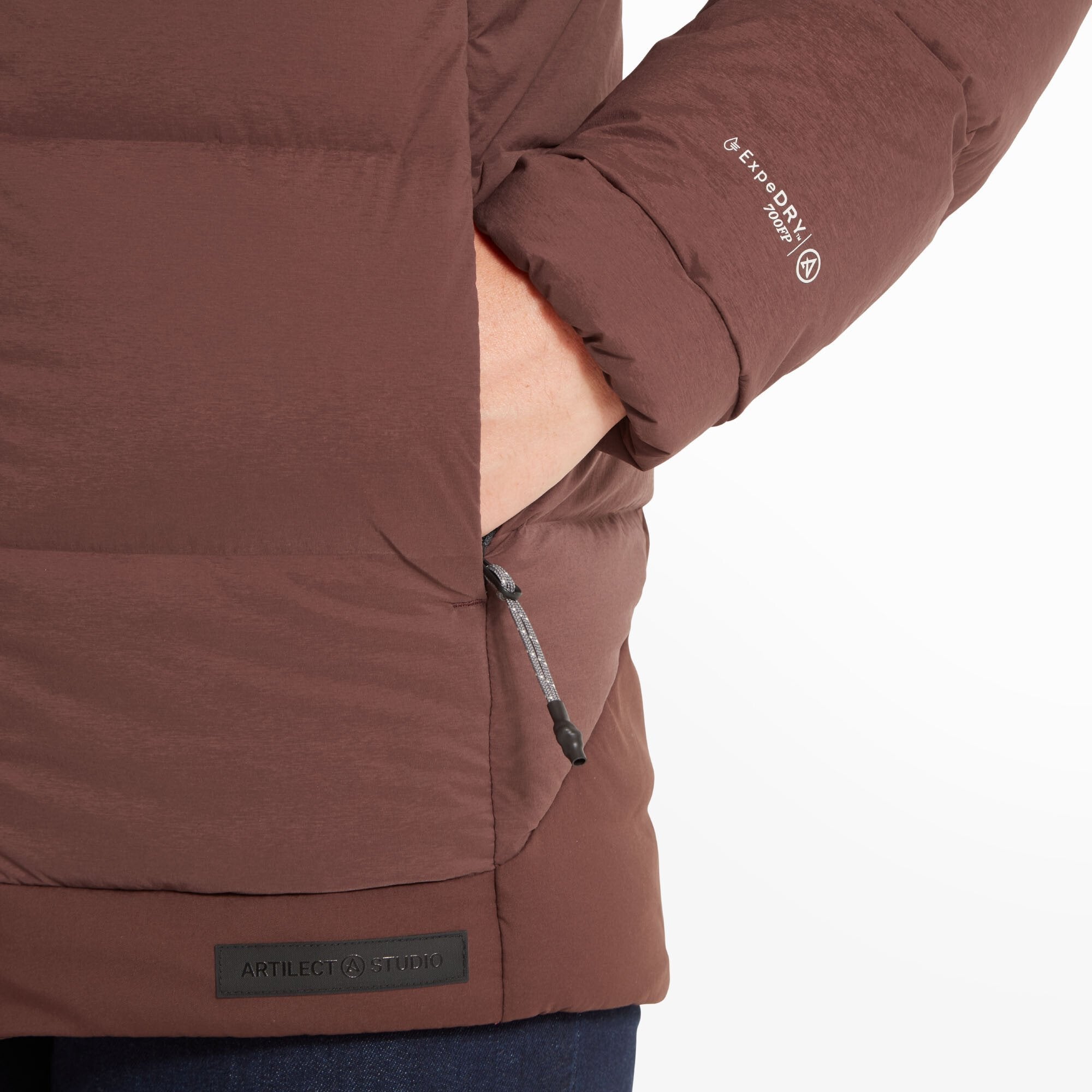 A hand is partially inserted into the side pocket on the Artilect Performance Womens High AF Down Stretch Parka Burgundy. The Artilect Studio patch is sewn at the hem, and "EXPEDRY 700FP" is printed in white on the sleeve.