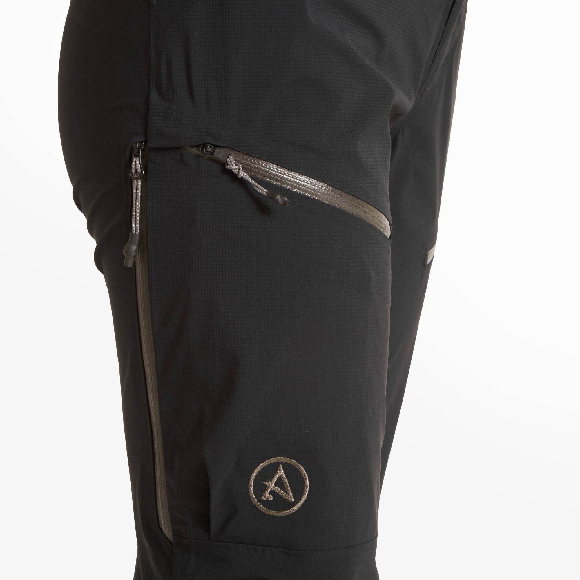 A close-up view of the left thigh area of the Artilect Performance Womens Kinetic Pant Black. The image highlights the two angled zippered thigh pockets and a subtle embroidered Artilect Systems logo in a muted gray tone. The zippers are waterproof and designed for technical outdoor use.