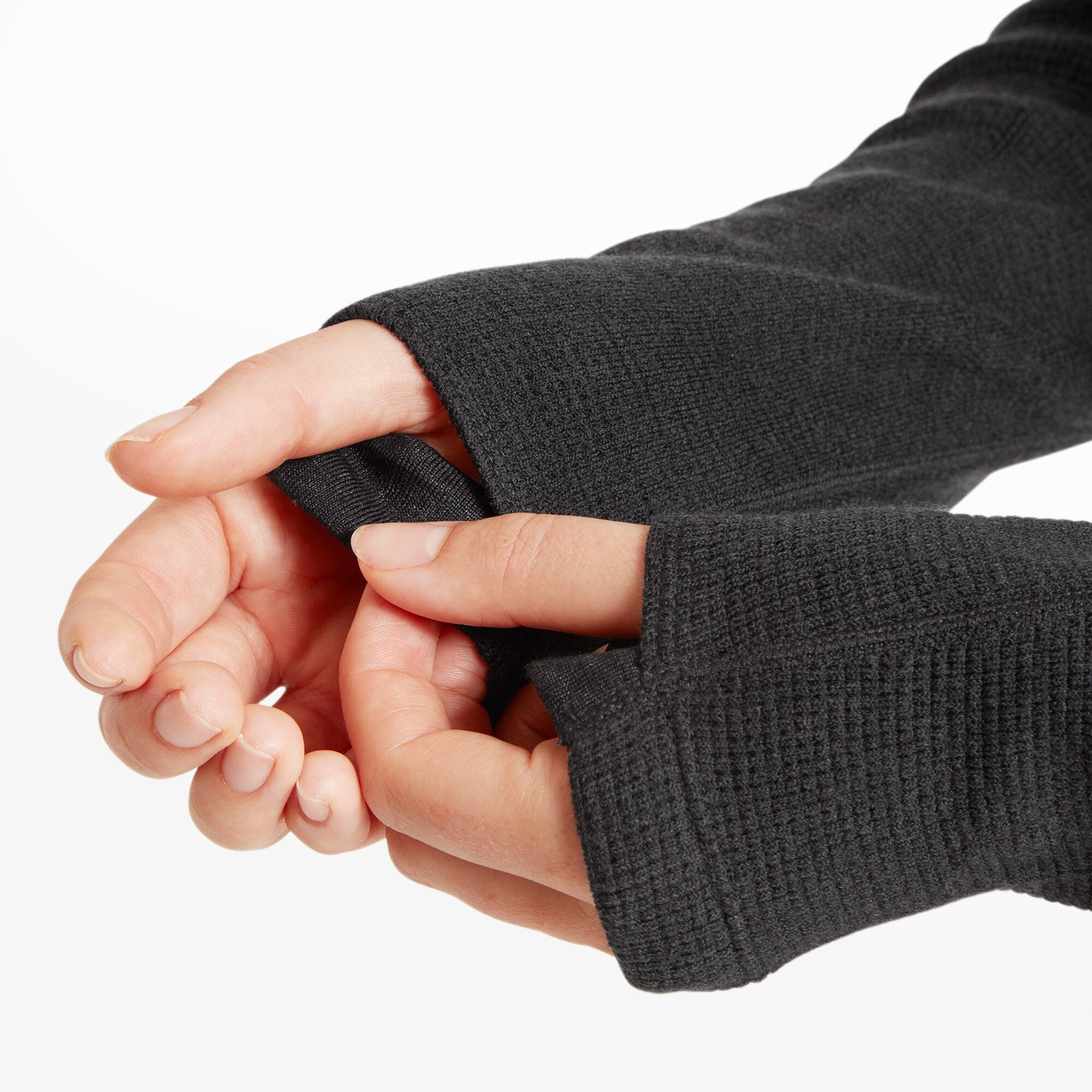 Image of the model’s hands pulling on the sleeves to show integrated thumbholes, designed for warmth and layering. The fabric’s grid texture is clearly visible on the Artilect Performance Womens Sundown 250 Half Zip Top Black.