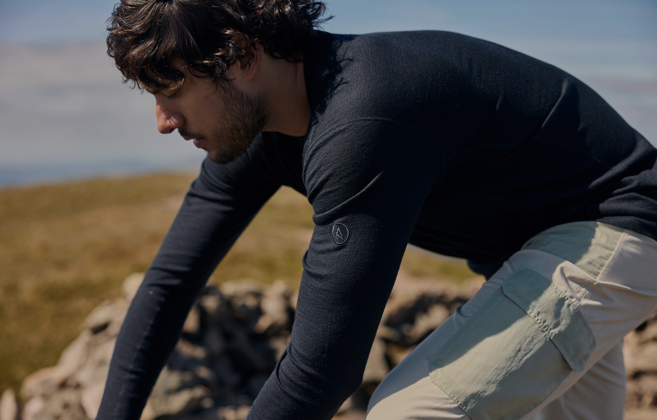 Man in dark long-sleeve shirt and light pants crouching on a rocky landscape with a blurred background