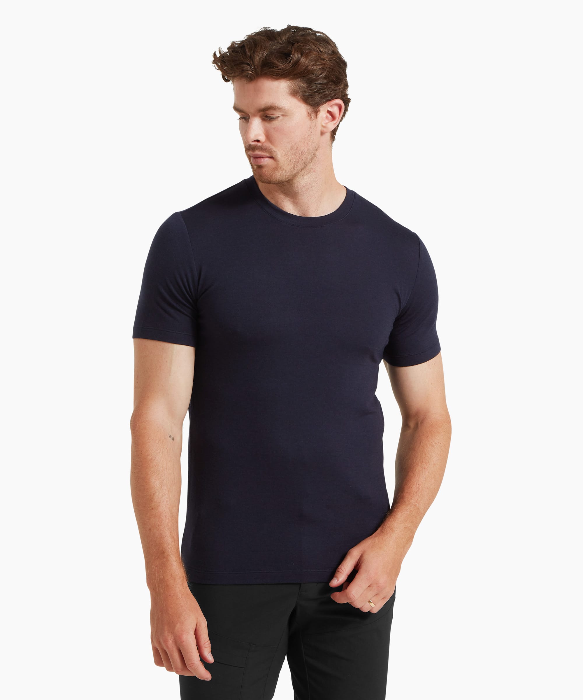 A man wearing a fitted navy short-sleeve T-shirt and black trousers, standing in a relaxed pose facing forward.