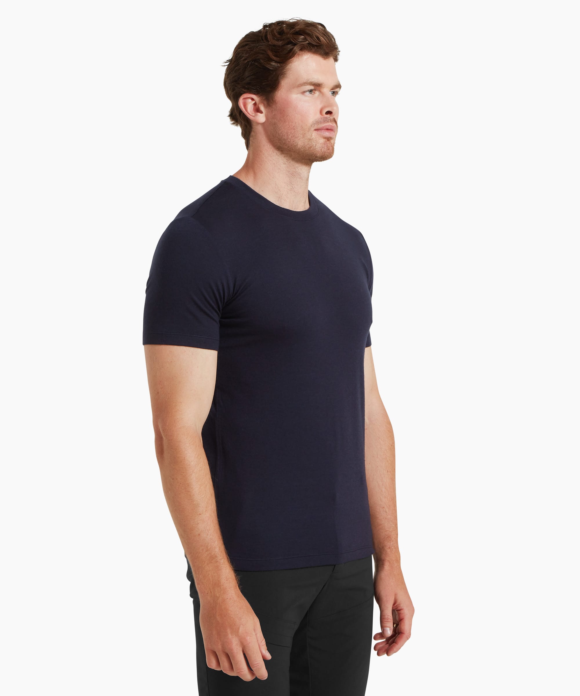 A man wearing a fitted navy short-sleeve T-shirt and black trousers, shown from a three‑quarter side angle against a plain white background.