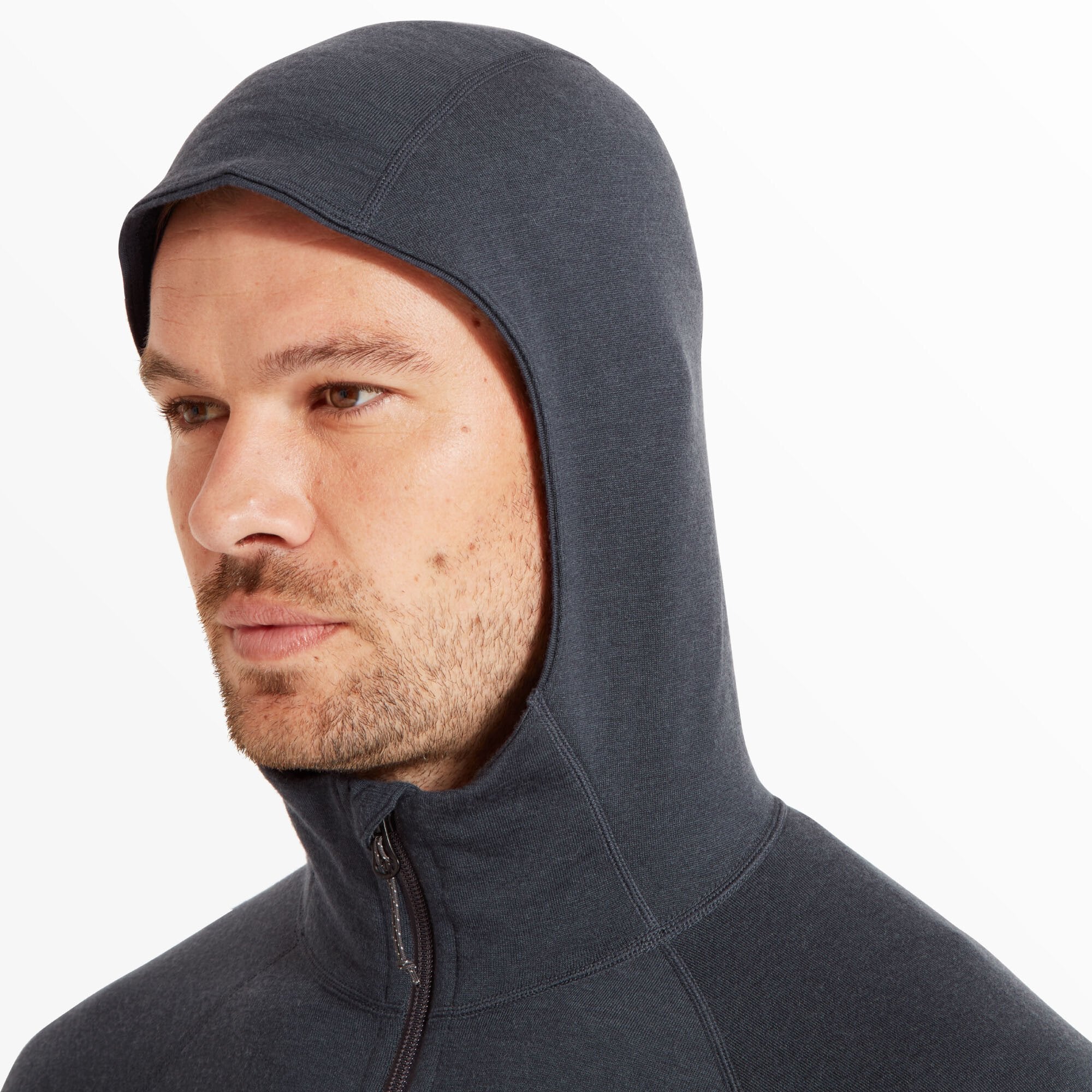 A close-up profile shot of the model wearing the hood up. The hood is snug-fitting and streamlined, providing full coverage of the head and neck. The fabric texture and seam detailing are prominent, emphasizing the Artilect Performance Mens Eldorado Merino Hoodie Blue’s technical design.