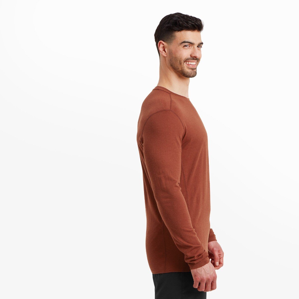 A left side profile of the model in the same Artilect Performance Mens Exposure Long Sleeve Tee Orange. This view highlights the clean side seam, shoulder stitching, and tailored fit through the torso and sleeves. The model maintains a slight smile while facing forward.