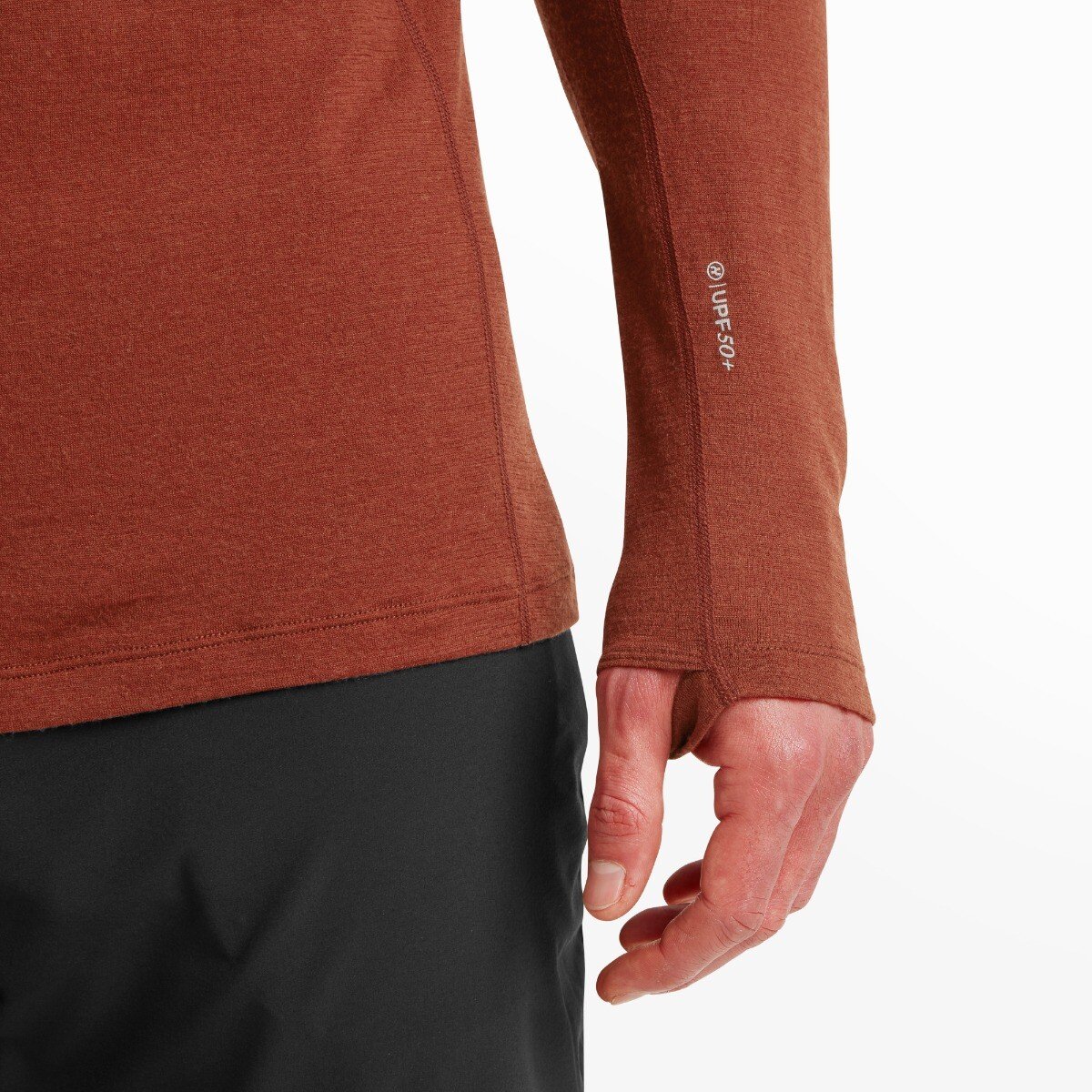A close-up of the lower sleeve and hip area on the Artilect Performance Mens Exposure Long Sleeve Tee Orange. The image focuses on the thumb hole feature in the cuff, worn by the model, and a printed “UPF 50+” label, indicating sun protection. The hemline stitching and contrast with black pants are also visible.