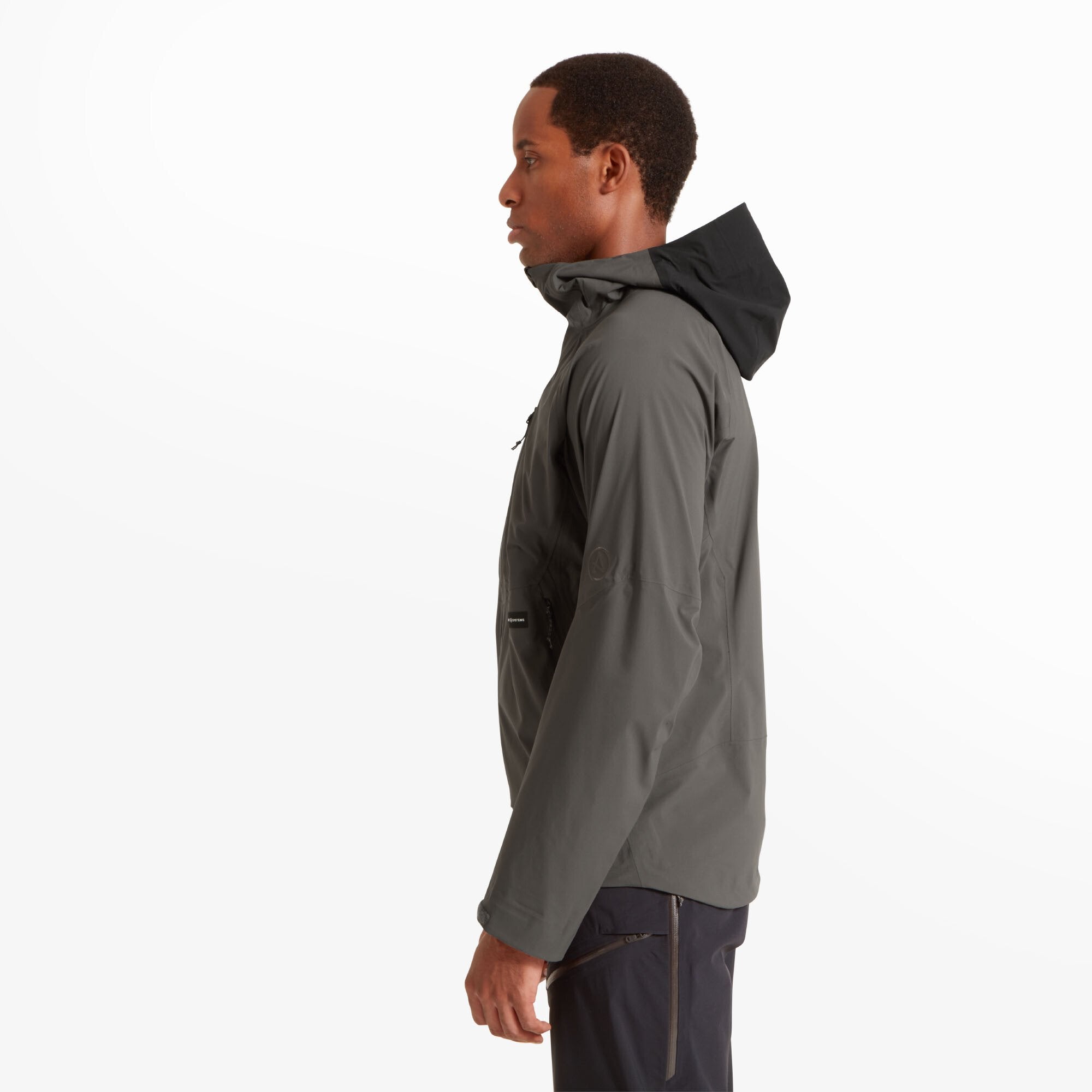 Side view of the model wearing the same Artilect Performance Mens Shadow Canyon Jacket Grey. The hood is up, and the sleeve shows subtle seam detailing. The profile highlights the jacket's slim, athletic fit and the smooth texture of the performance fabric.