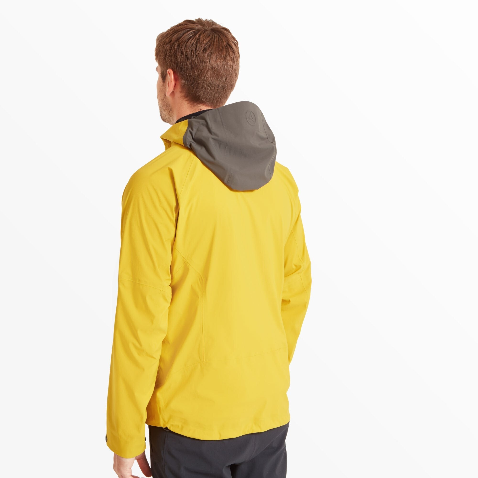 The model is facing away, showing the back of the Artilect Performance Mens Shadow Canyon Jacket Yellow. The hood is down, revealing its contrasting dark grey inner fabric. The jacket has a clean back with minimal seams for a sleek silhouette.