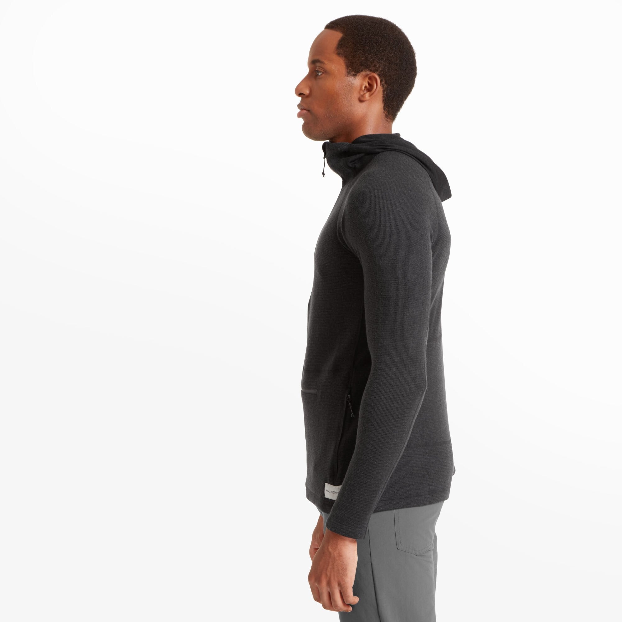 A side view of the man showcasing the Artilect Performance Mens Sundown 250 Half Zip Top Black’s slim fit. The hood rests flat against the back, and the fabric conforms closely to the body. The structured design emphasizes the garment’s athletic fit.