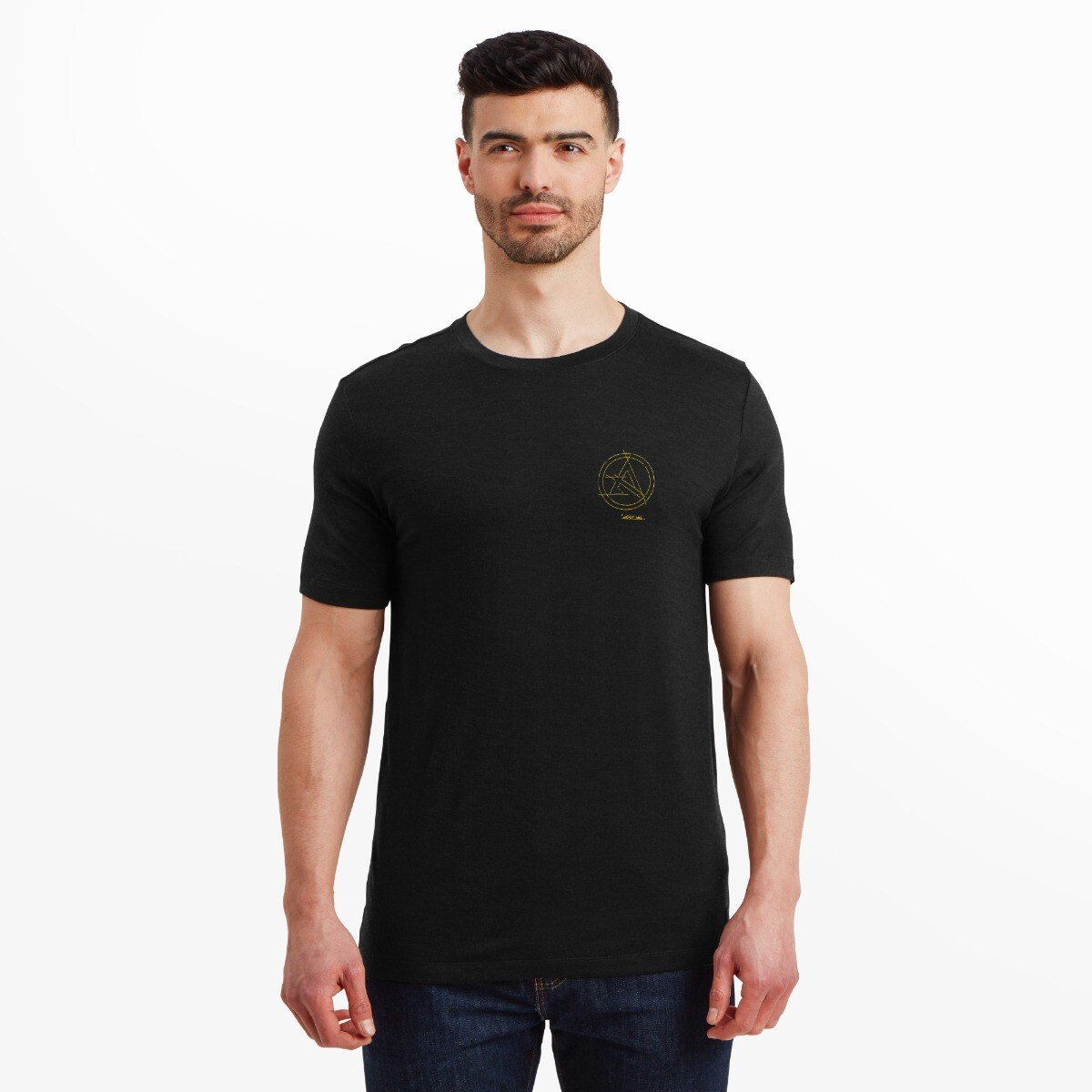 A man wearing a fitted, short-sleeve, Artilect Performance Mens Utilitee Draft Black with a small yellow geometric logo printed on the left chest. The shirt is paired with dark blue jeans, and the model stands facing forward with a neutral expression against a white background.