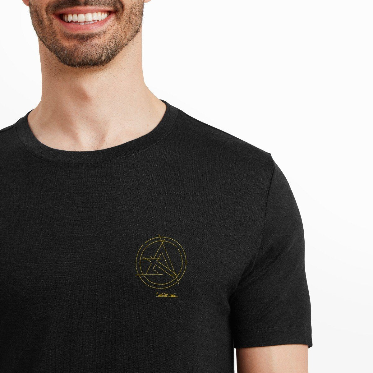 A cropped view showing the upper torso of the model, focusing on the yellow geometric Artilect logo on the left chest of the Artilect Performance Mens Utilitee Draft Black. The fabric texture is visible, and the shirt collar appears finely stitched and well-fitted.