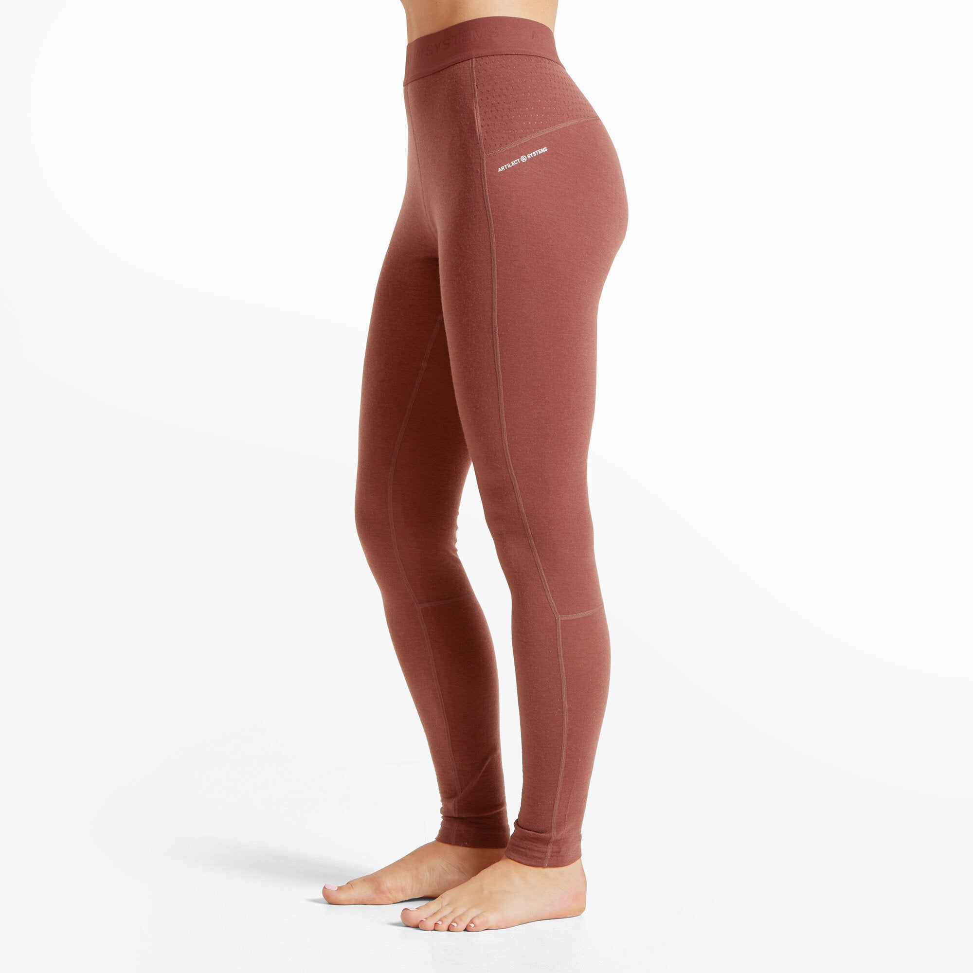 A side profile view of a woman wearing the Artilect Performance Womens Boulder 125 Legging Burgundy, showcasing the contouring design and seams running down the legs. The leggings have a smooth and stretchy fit.