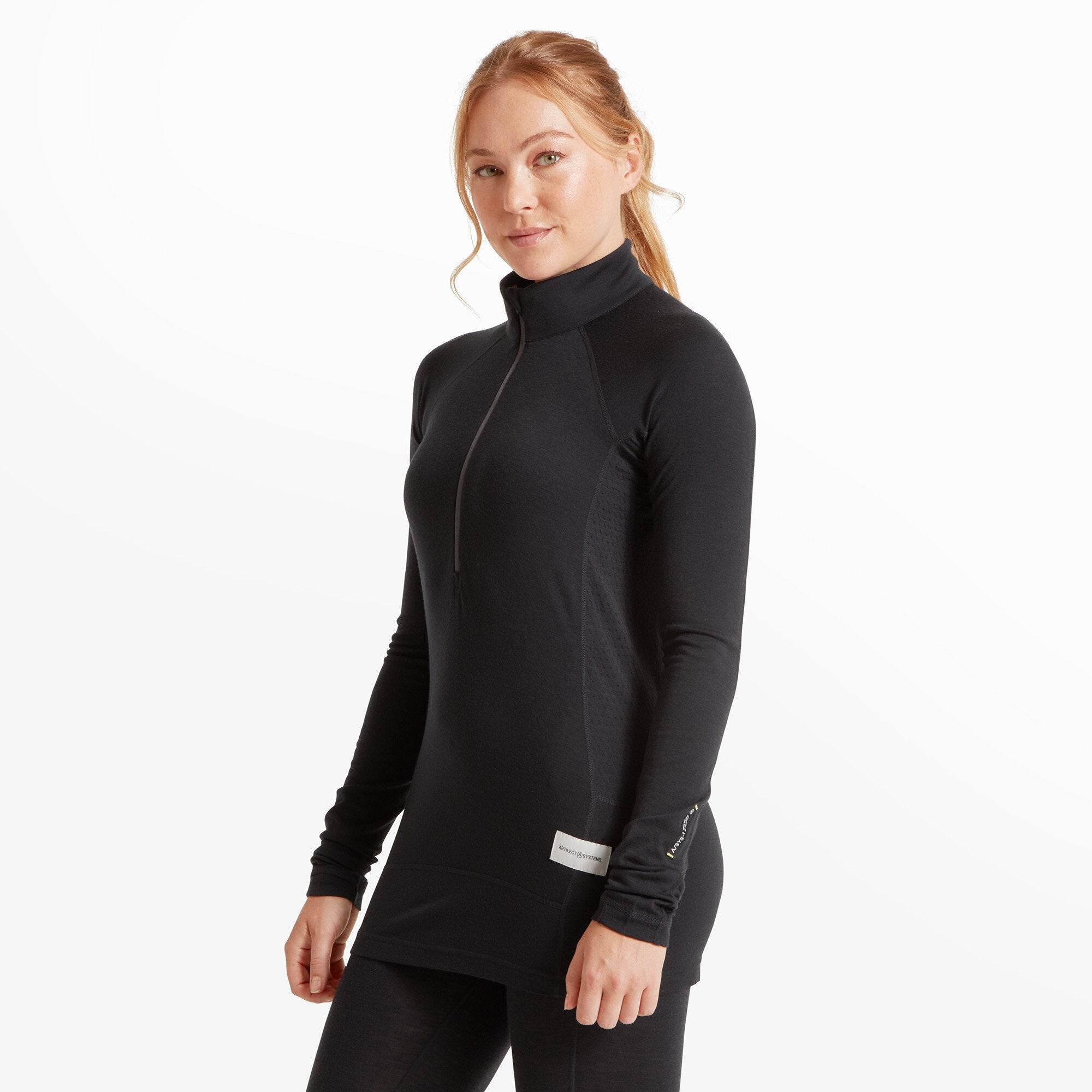 The same woman is shown in a three-quarter profile view, turned slightly to the right. The Artilect Performance Womens Boulder 125 Quarter Zip Top Black snugly fits her form, emphasizing the contours of the performance fabric. The left sleeve features a small black label with text. The high collar is zipped up, and the model maintains a calm and confident expression.