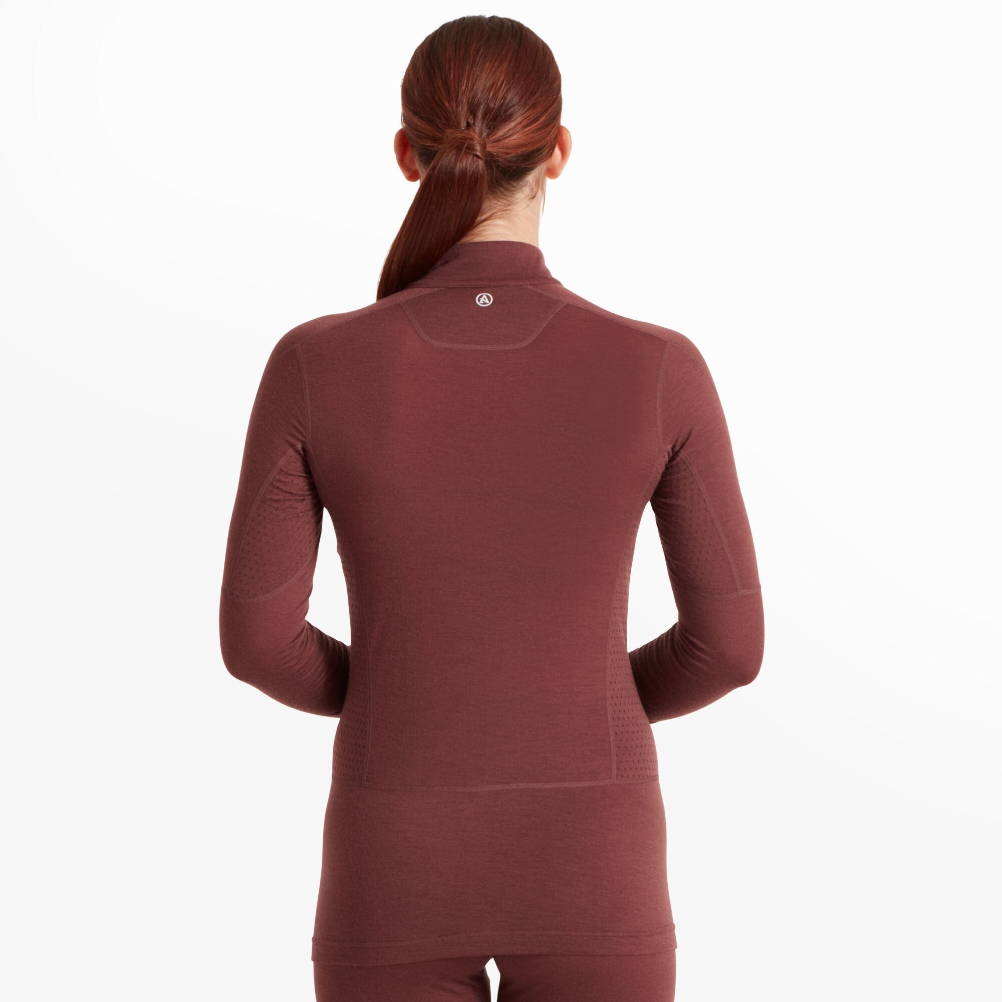 The model is turned around, showing the back of the Artilect Performance Womens Boulder 125 Quarter Zip Top Burgundy. The back panel has subtle stitching details, and the brand’s circular logo is positioned near the collar. The long hem provides additional coverage.