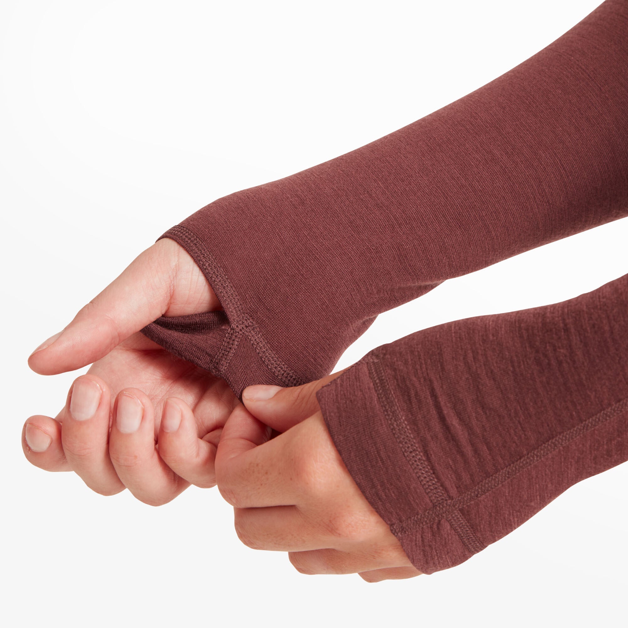 The model is demonstrating the thumbholes in the sleeves by pulling them over her hands on the Artilect Performance Womens Boulder 125 Quarter Zip Top Burgundy. The thumbholes are reinforced with stitching, and the fabric appears flexible and comfortable.