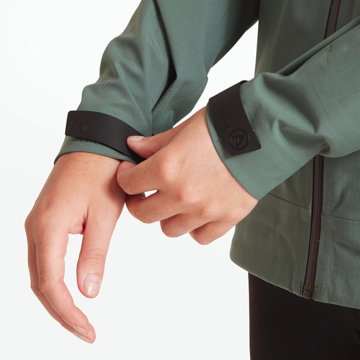 A close-up of the model adjusting the Velcro cuff tab on her wrist, revealing the tailored sleeve and smooth fabric finish. This emphasizes the Artilect Performance Womens Grandview 3L Jacket Green’s adjustable fit.