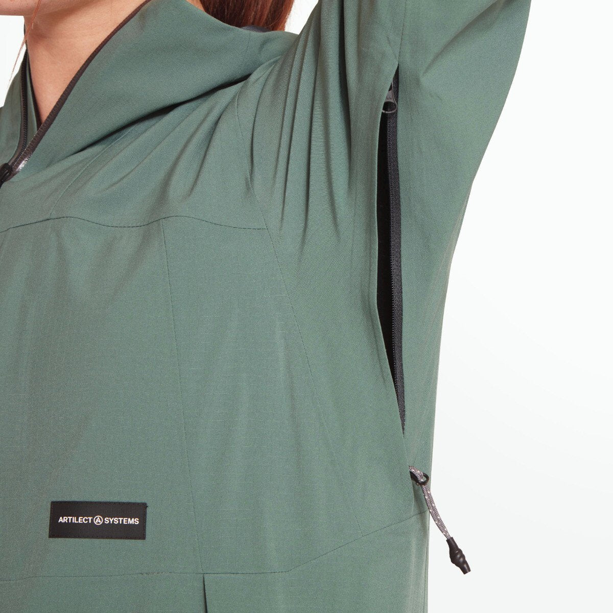 A close-up of the pit zip, partially unzipped, showing the hidden ventilation option for increased breathability. This image captures the functional aspect of the Artilect Performance Womens Grandview 3L Jacket Green’s underarm design.