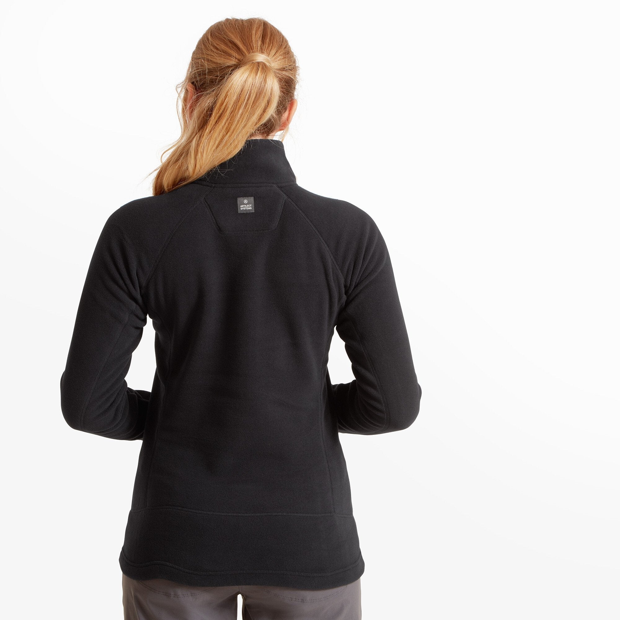 Back view of the woman wearing the Artilect Performance Womens Halfmoon Bio Pullover Black. The curved seam lines and the Artilect Systems logo tag centered near the top back of the collar are visible. Her blonde ponytail rests just above the collar.