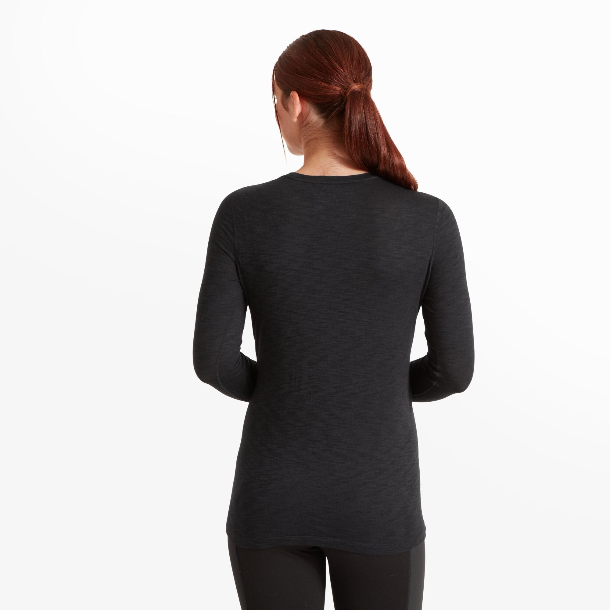 Back view of the woman in the same Artilect Performance Womens Sprint Long Sleeve Tee Black. The shirt extends slightly past the hips, providing full coverage. The back is seamless and free from branding, highlighting the clean design and the smooth fit over the shoulders and back.