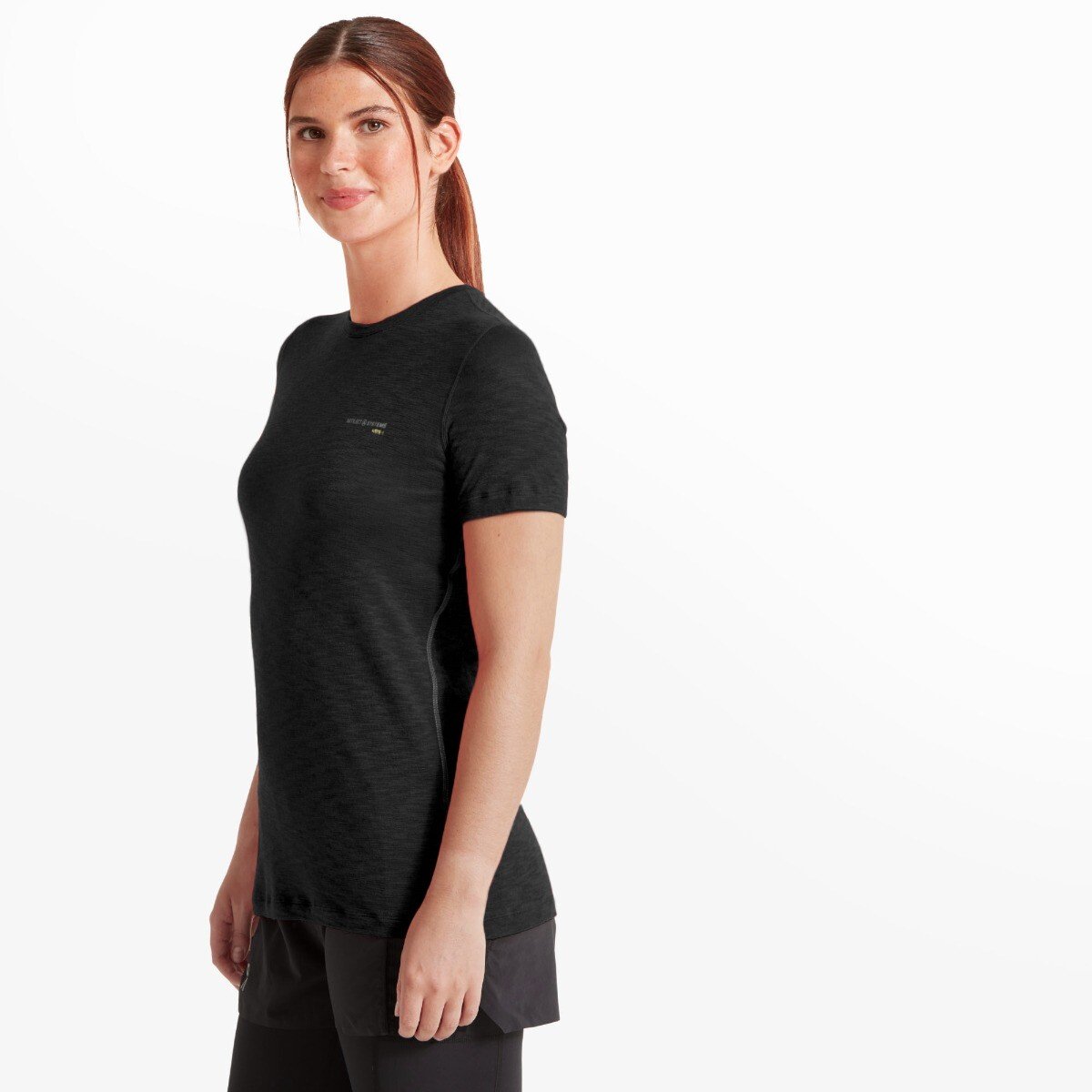 A three-quarter side view of the woman in the same Artilect Performance Womens Sprint Tee Black, showing the contoured fit and clean side seams. Her posture is upright and confident, with her arms relaxed at her sides. Subtle flatlock stitching can be seen along the side of the shirt, emphasizing the athletic design. The logo remains visible on the chest from this angle.