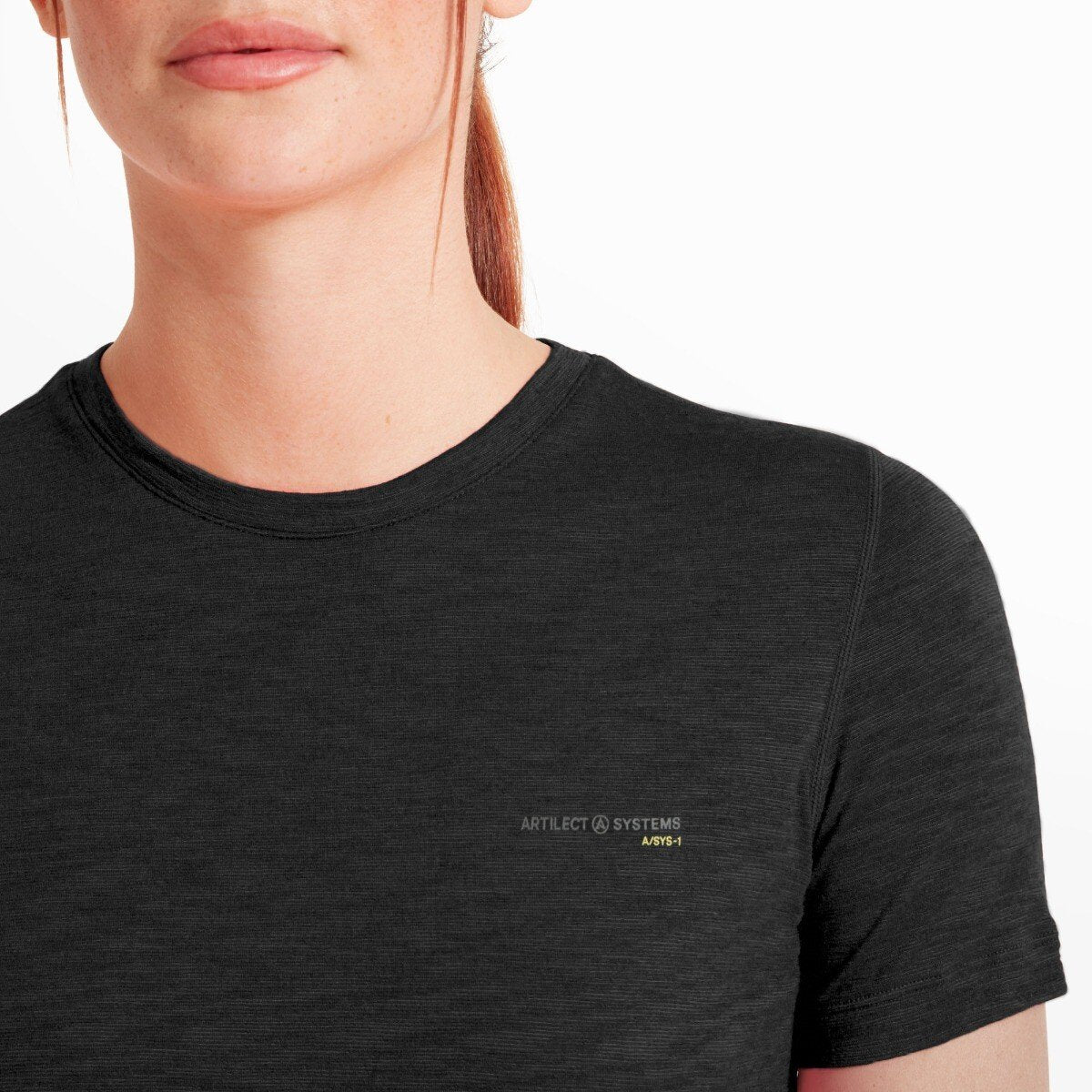 A close-up image of the upper chest and neckline area of the Artilect Performance Womens Sprint Tee Black. The soft, crew neckline lies flat against the skin. The logo "ARTILECT SYSTEMS ASYS-1" is clearly printed on the left chest in subtle gray with a pop of yellow. The merino blend fabric’s fine, smooth knit is visible in detail.