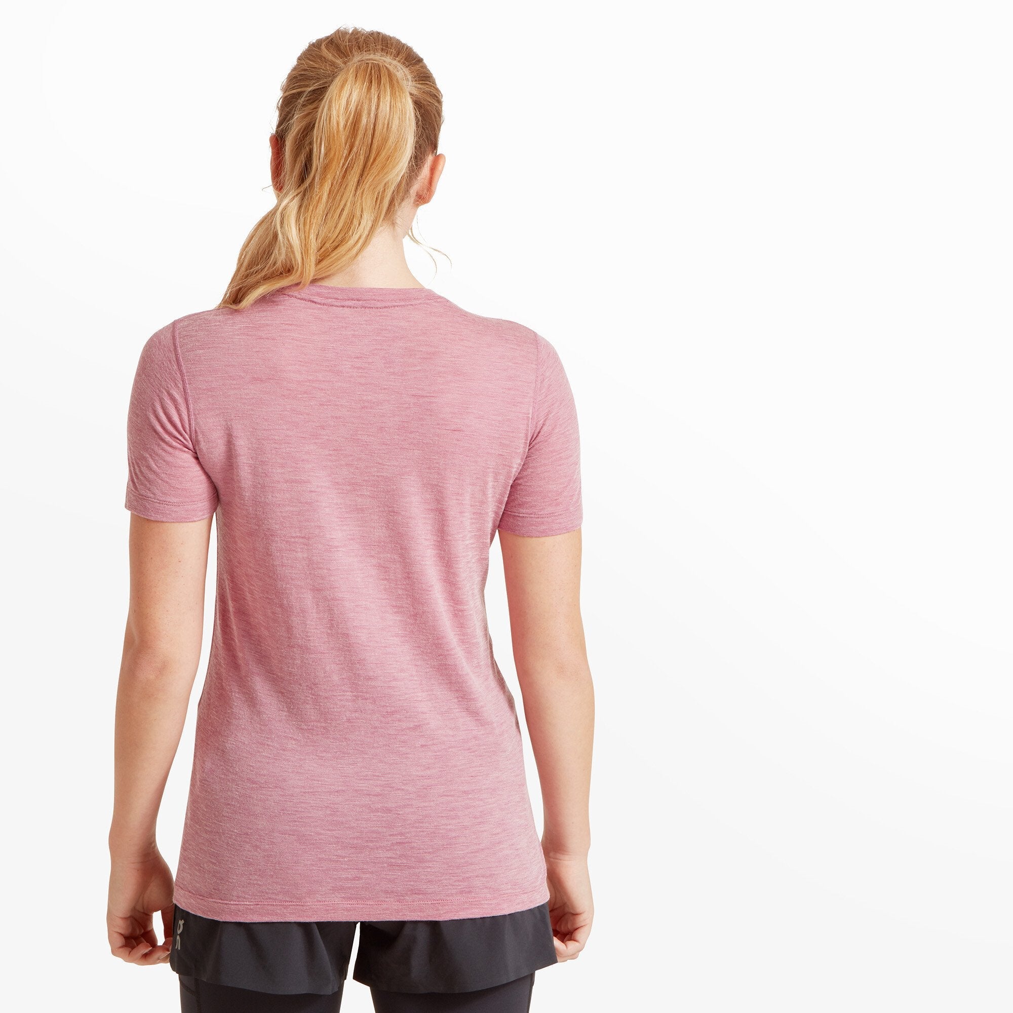 Back view of the woman showcasing the rear design of the Artilect Performance Womens Sprint Tee Pink. The shirt has a simple, seamless back with no logos or additional detailing. The hem curves slightly around the hips. Her blond ponytail rests neatly against the upper back of the shirt, and the shoulder seams align cleanly.