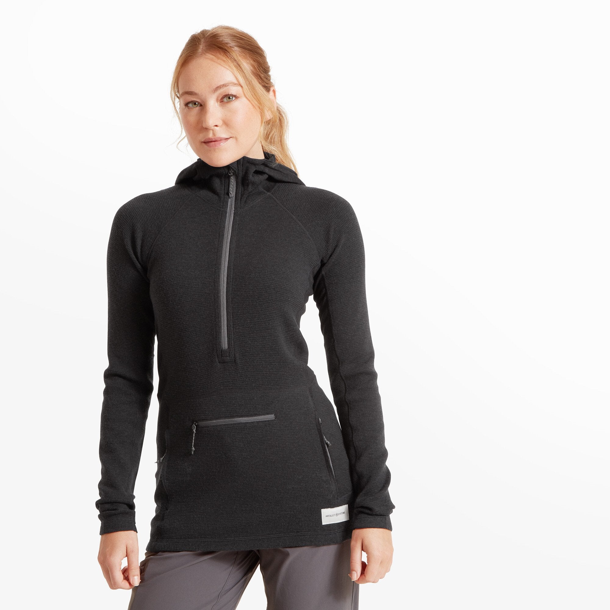 A woman wearing a Artilect Performance Womens Sundown 250 Half Zip Top Black, standing facing forward. The top has a streamlined athletic fit with long sleeves, a chest zipper reaching up to the high neck, and visible panel seams.