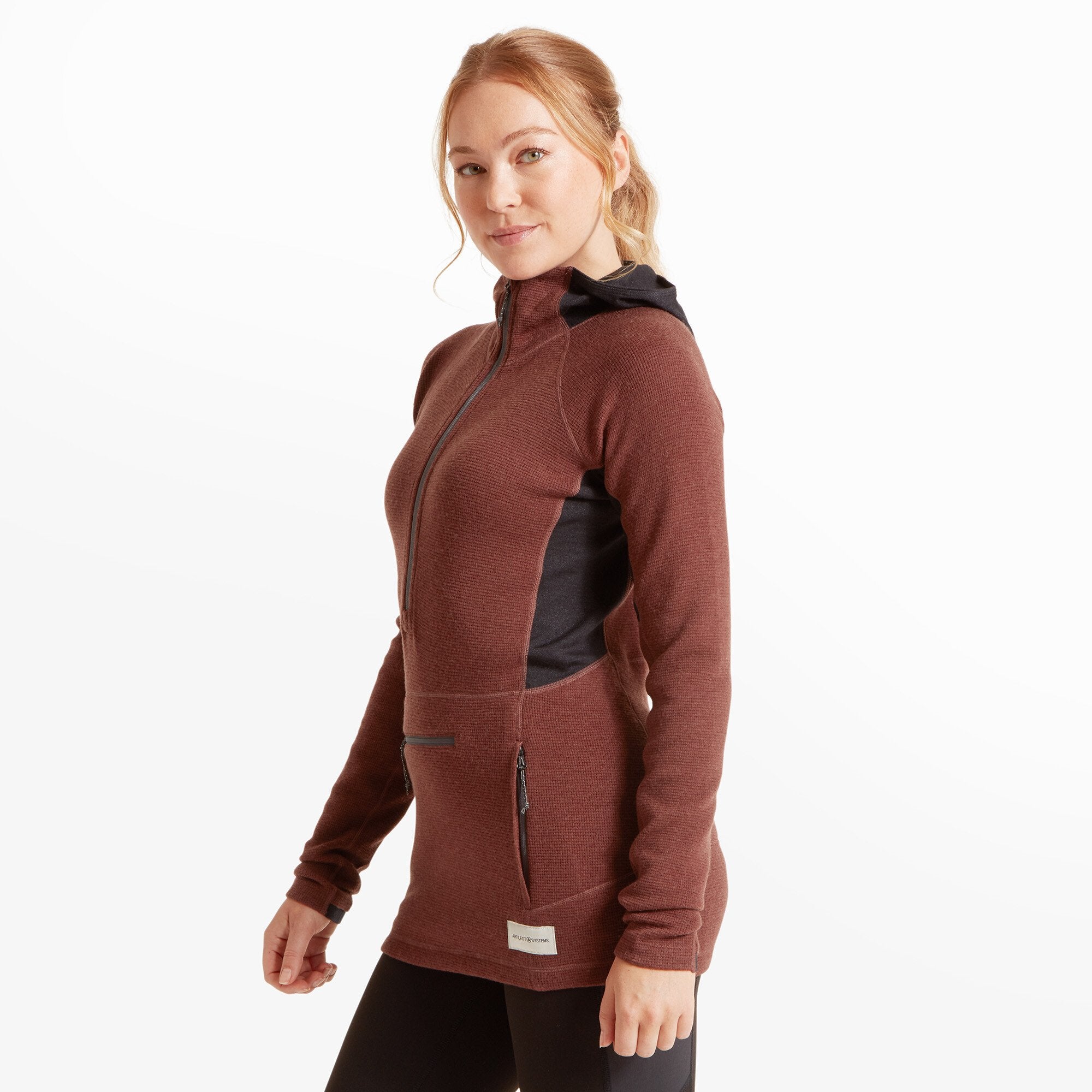A back view of the woman wearing the Artilect Performance Womens Sundown 250 Half Zip Top Burgundy. Her long hair is tied back in a ponytail, revealing the attached black hood. The hood features a small label that reads "ASYSS-2™" in yellow and white text. The side panel seams and fitted shape are clearly shown.