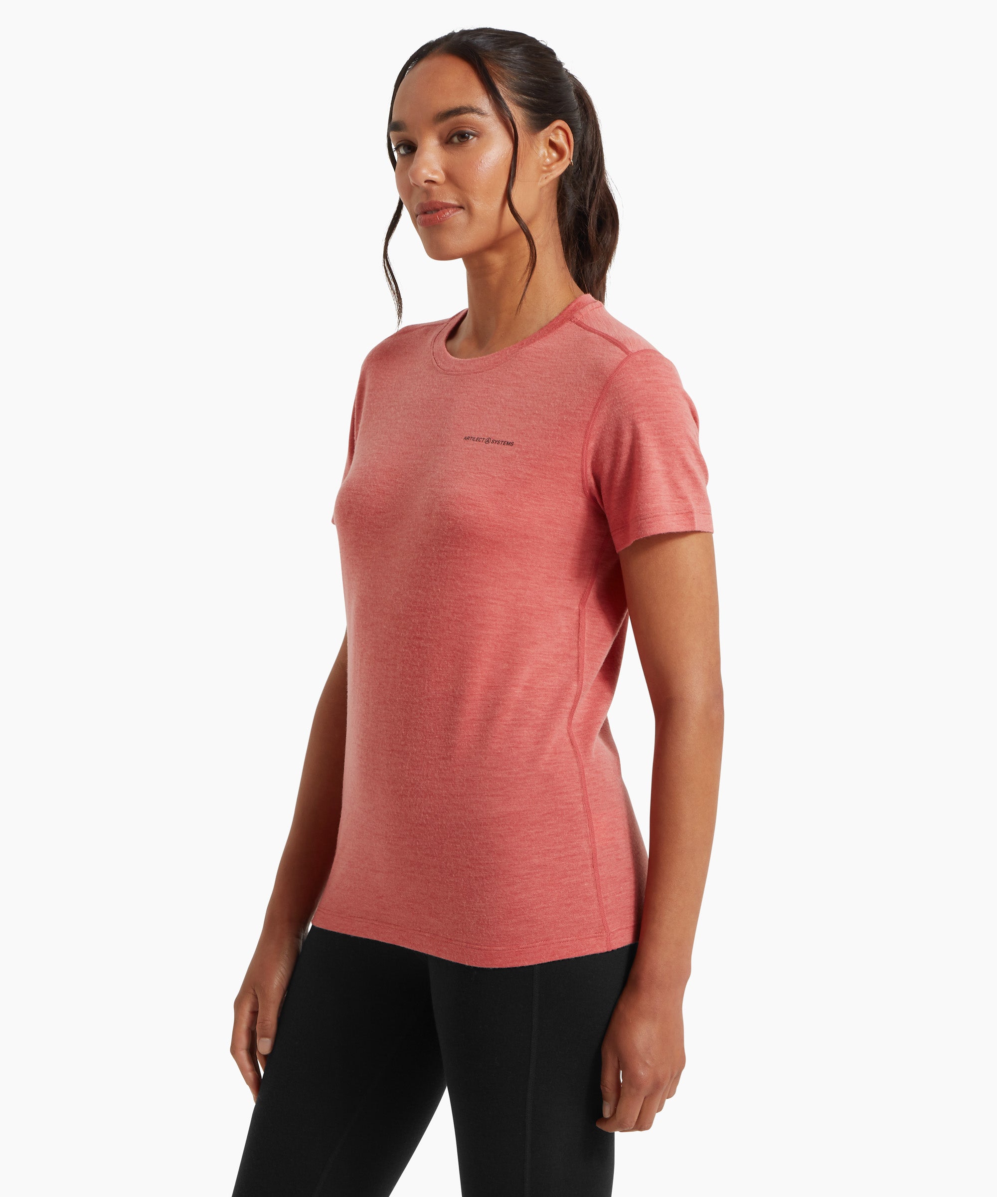 A woman wearing a fitted coral‑pink short‑sleeve T‑shirt and black leggings, shown from a three‑quarter side angle against a white background.