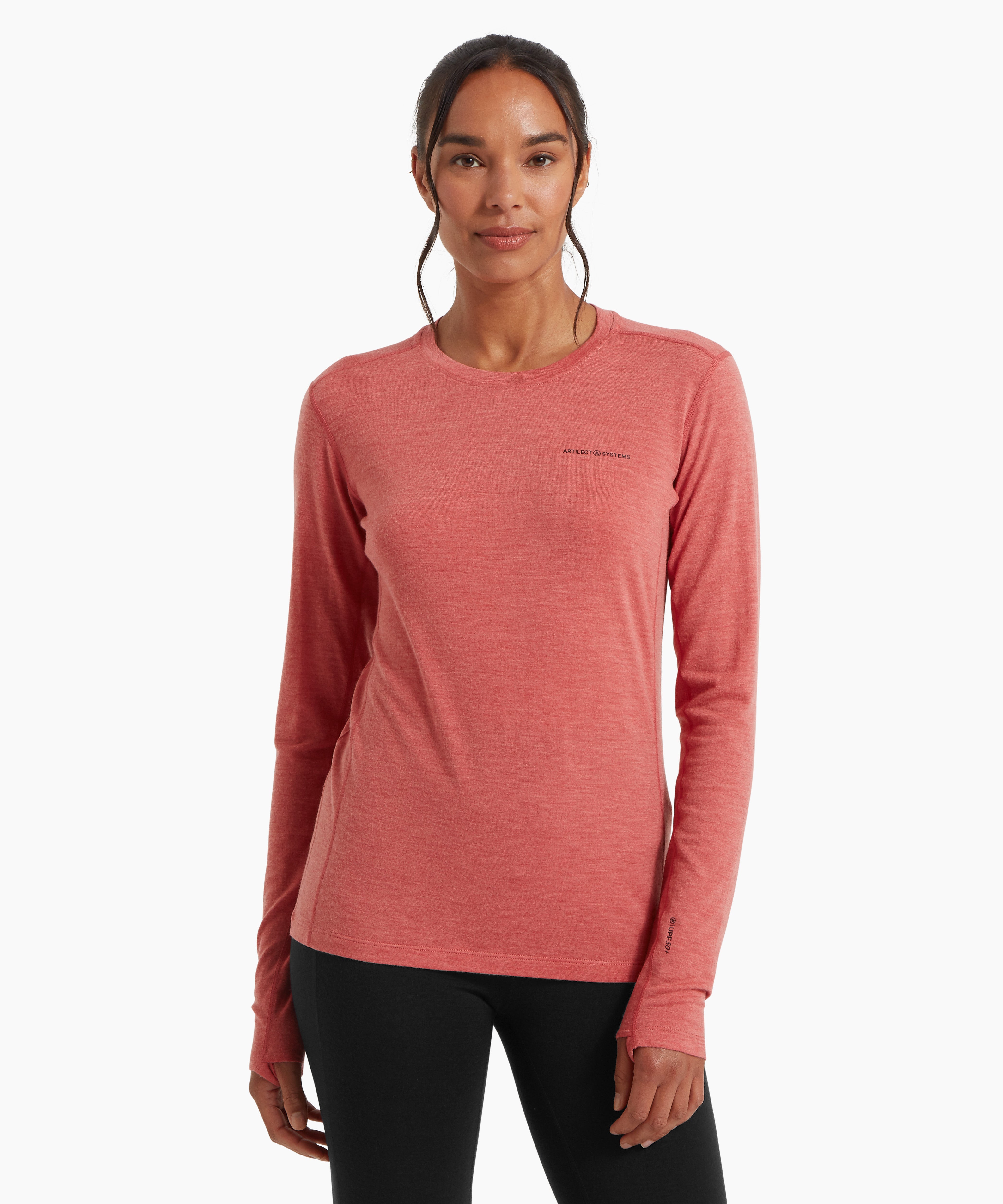 A woman wearing a fitted coral‑pink long‑sleeve top and black leggings, standing in a relaxed front‑facing pose against a white background.