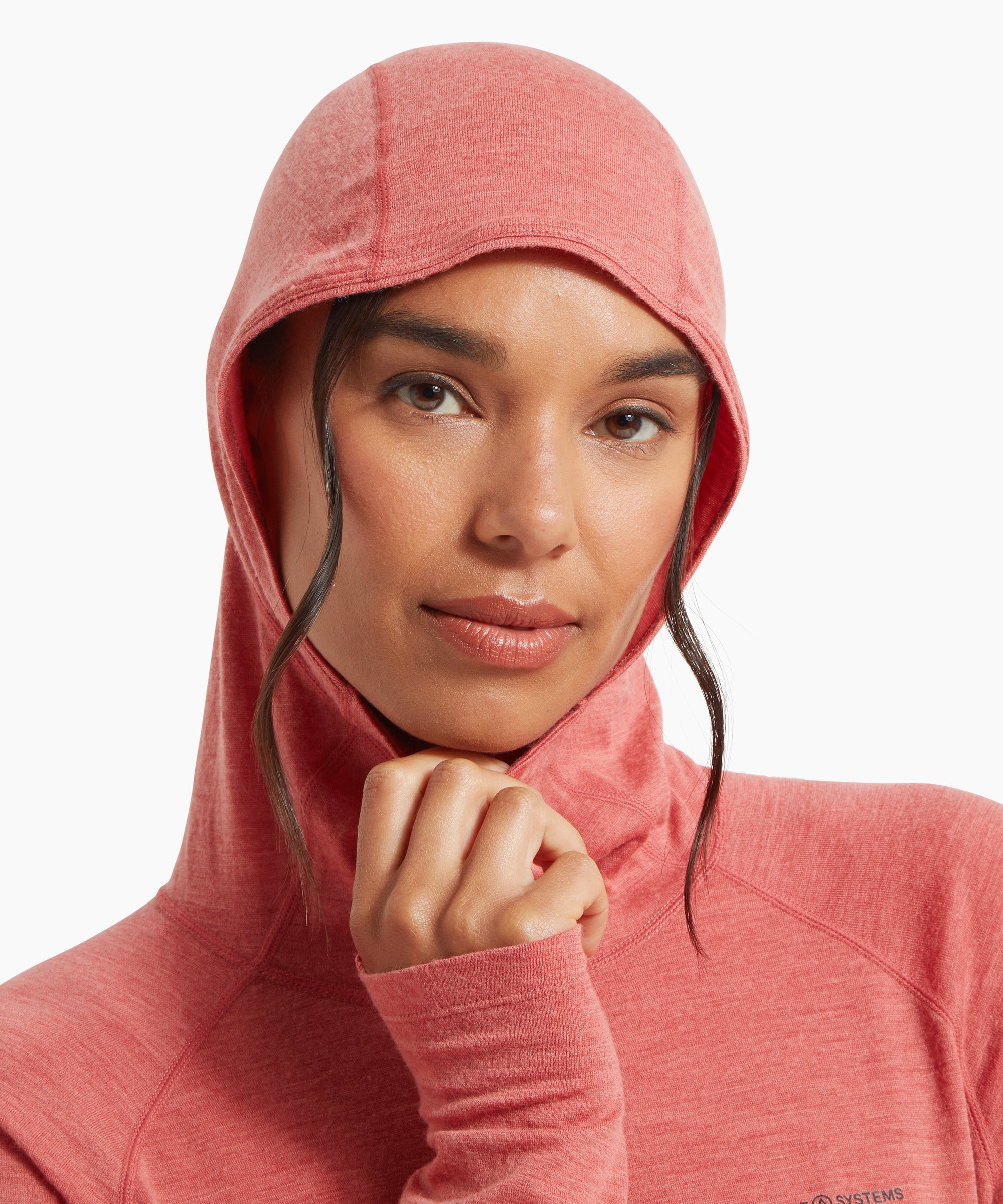 A close-up of a woman wearing a coral‑pink lightweight hooded top, shown with the hood pulled up and one hand holding the collar. The soft, textured fabric is visible.